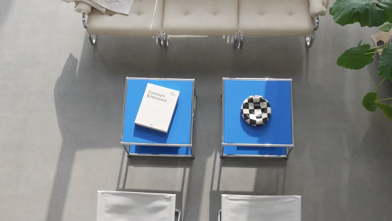 Draufsicht auf USM Haller Tische in Blau mit Buch und Schale in modernem Wohnzimmer mit hellem Sofa und Pflanzen.